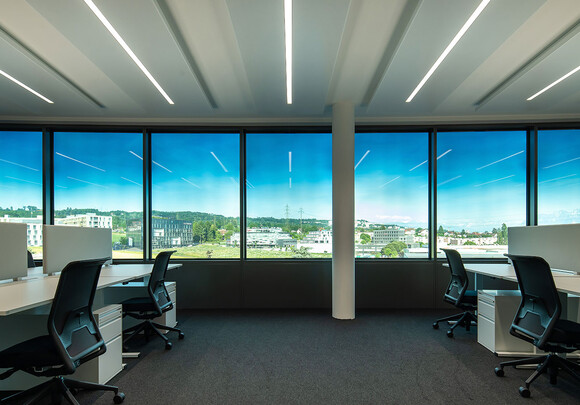 Collaborative office space with smart glass windows from left to right overlooking a town. 