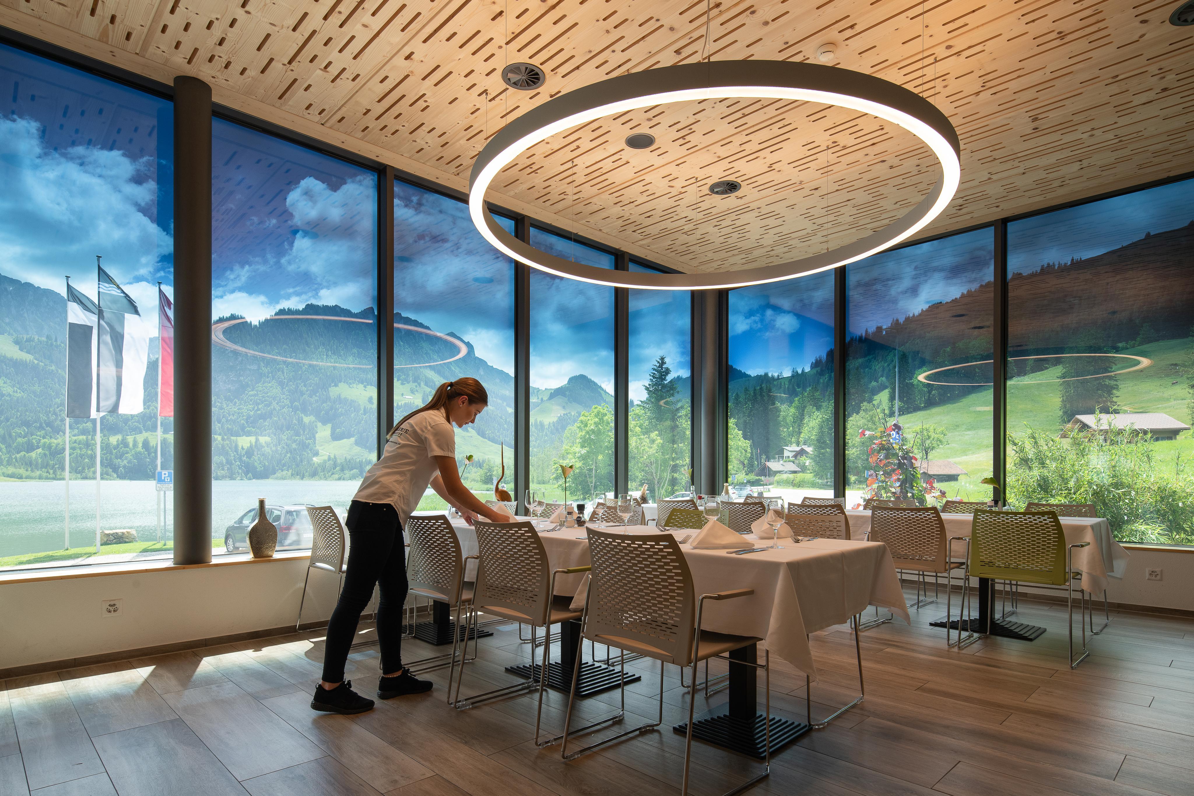 Woman setting dining table in a room with custom smart glass windows overlooking mountain range. 