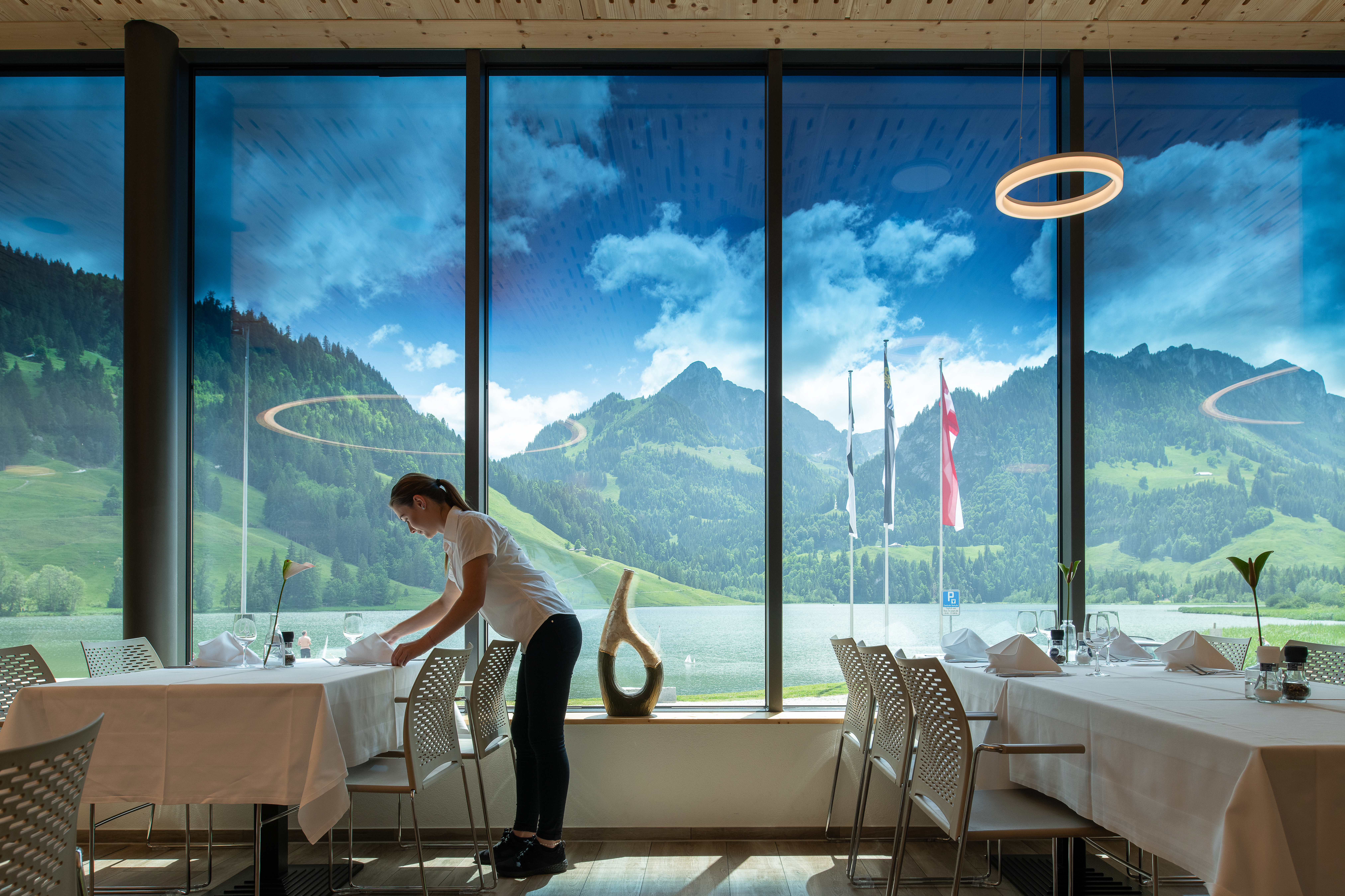 Picture showing the Schwarzsee Restaurant with the mountains on the background. A women is setting the tables.