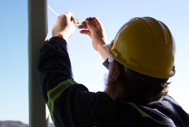 Construction worker holding electrical connection in the air with a shot of the sky in the background. 