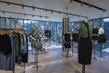 Inside a clothing store with women's fashions. Behind the clothing is a glass wall.