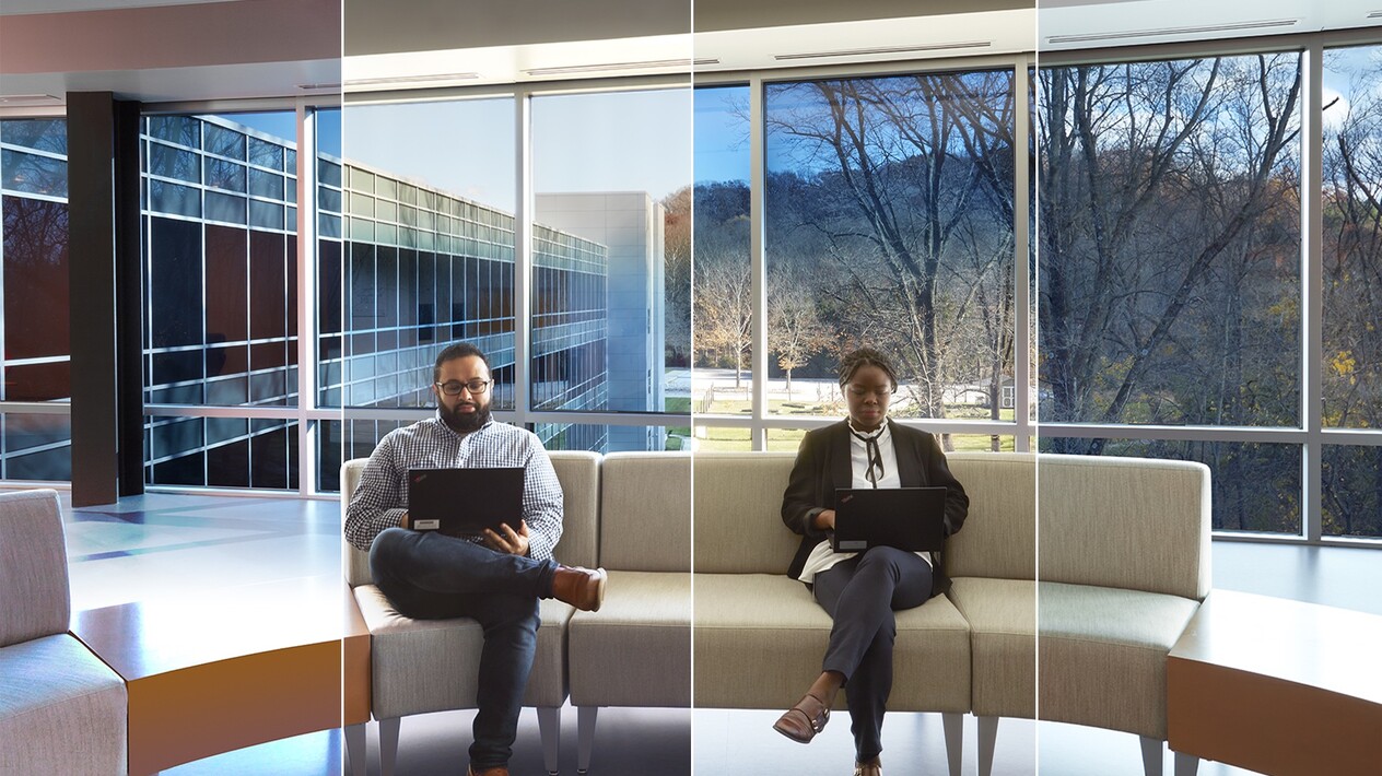 Two coworkers sitting on couches in the common with smart glass windows from left to right behind them.