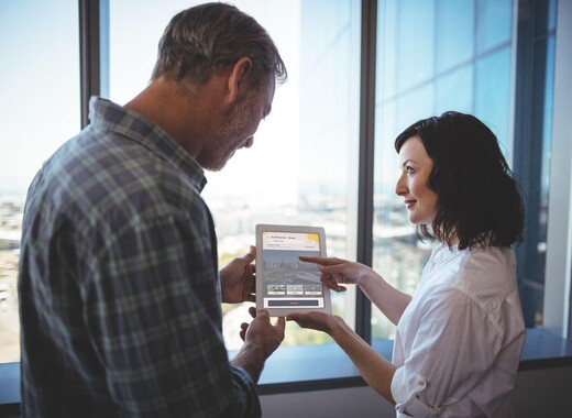 Man and woman looking at a tablet in front of smart glass windows. 
