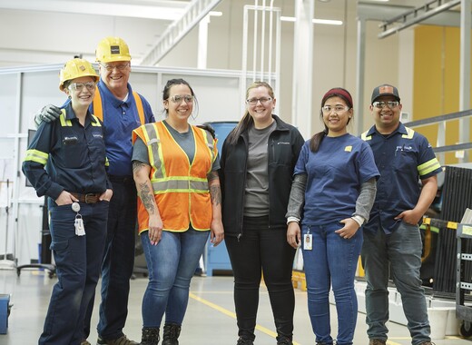 Six SageGlass employees in workwear and safety glasses collaborating in a manufacturing plant.