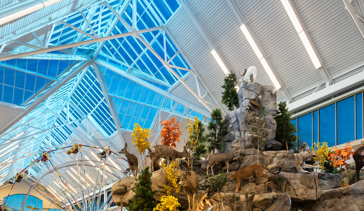 A glass atrium at Scheels housing a ferris wheel and a fake mountain with taxidermy wildlife and trees scattered around it.
