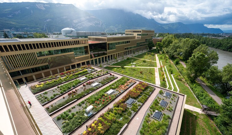 Beautiful exterior shot of the side and top of a building that has lots of plants growing on the roof. There are mountains in the background.