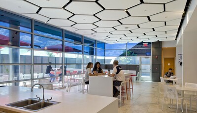 Interior of an modern smart glass building with large windows and a groups of people eating lunch at tables.