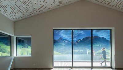 Interior space of a home with smart glass windows overlooking mountains with woman walking on deck. 