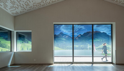 Interior space of a home with smart glass windows overlooking mountains with woman walking on deck. 