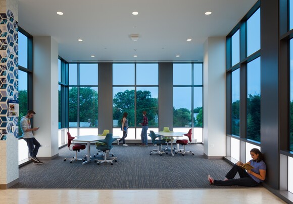 Interior common space of office building with huge smart glass windows from left to right and people hanging out. 