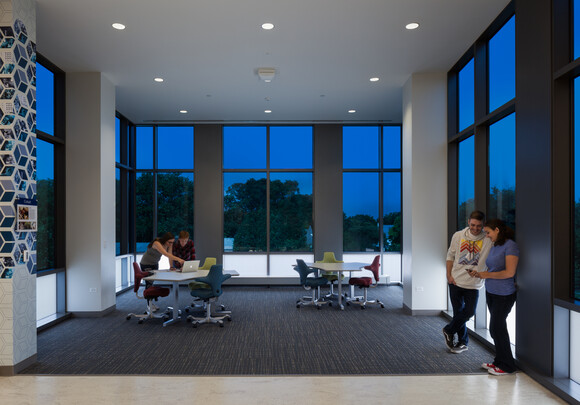 Common working space with coworkers collaborating at a table and surrounded by smart glass windows. 