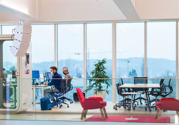 Interior of an modern building with large smart glass windows and a coworking space with people working on their computers.