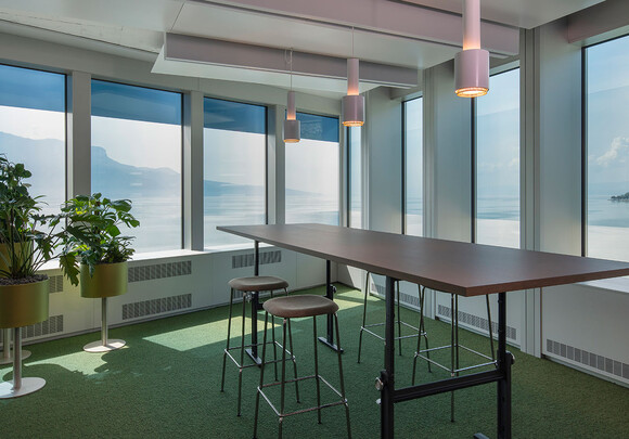 Interior of meeting room with high top table and smart glass windows overlooking the water and mountains. 