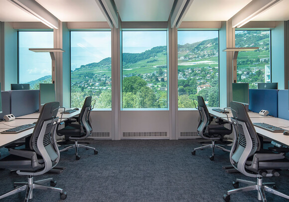 Collaborative office space with smart glass windows from left to right overlooking a mountain side. 