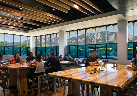 Interior of dining hall with people eating with smart glass windows from left to right overlooking mountain range.